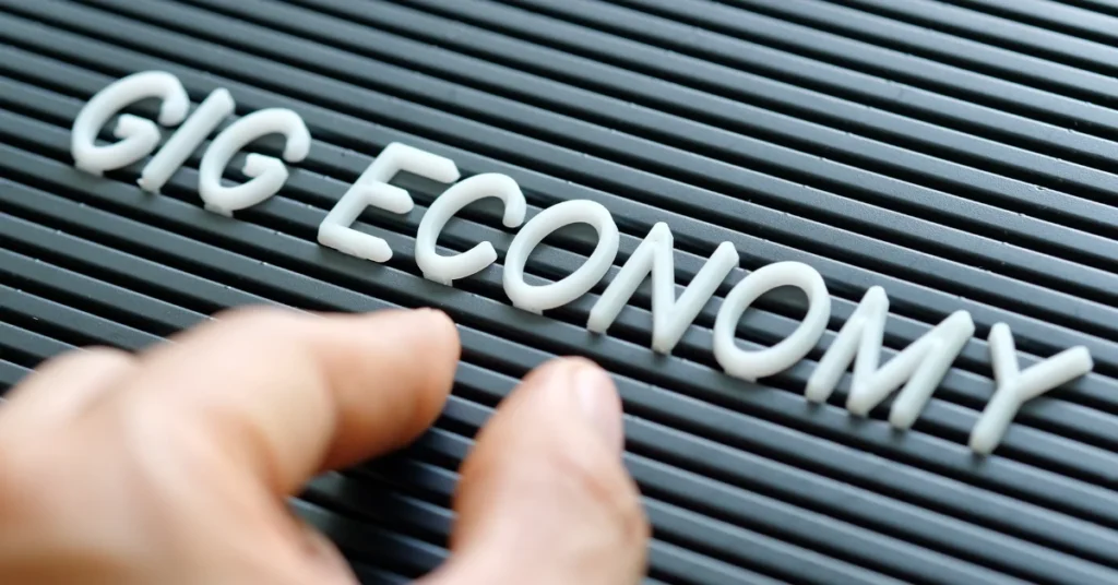 Close-up of hand placing letters spelling "GIG ECONOMY" on a sign board